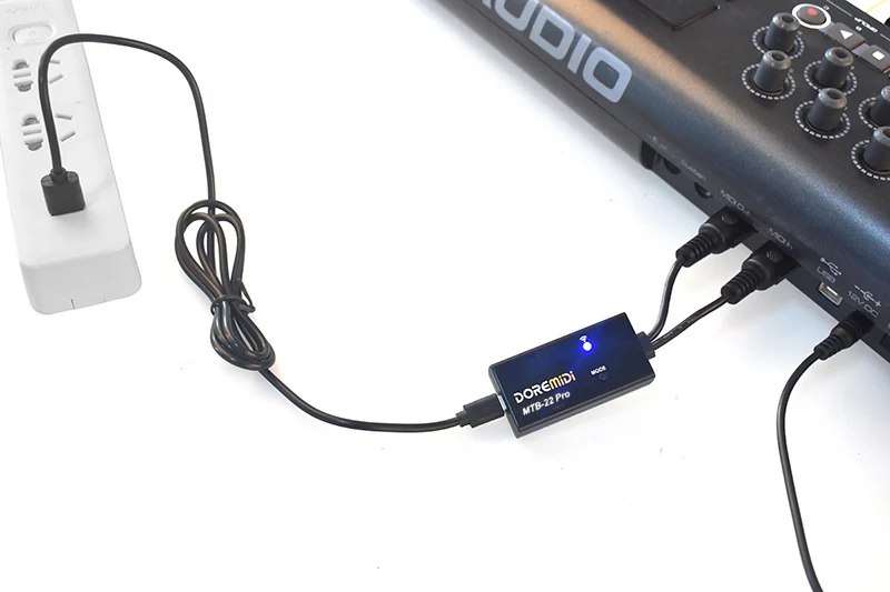DOREMiDi MTB-22 Bluetooth MIDI adapter plugged into a keyboard's MIDI ports, blue LED on